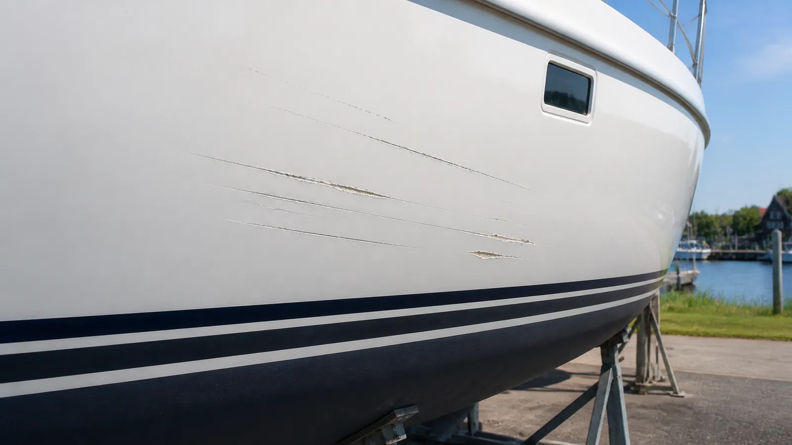 Krassen en schuurplekken in de witte gelcoat van een romp, vlak boven de donkere waterlijn